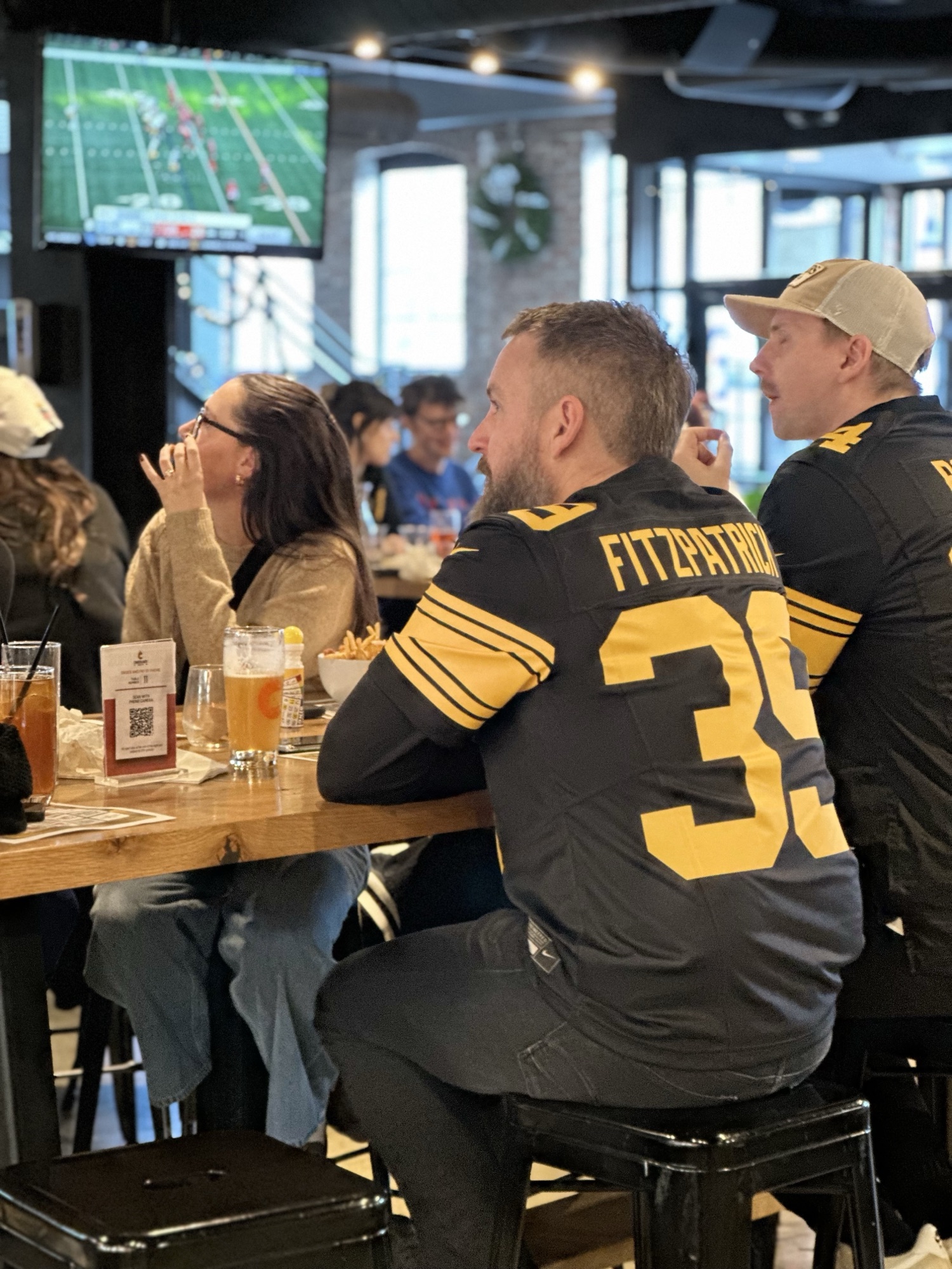 Fans in Steelers jerseys watching the game on the big screen at Cinderlands Warehouse
