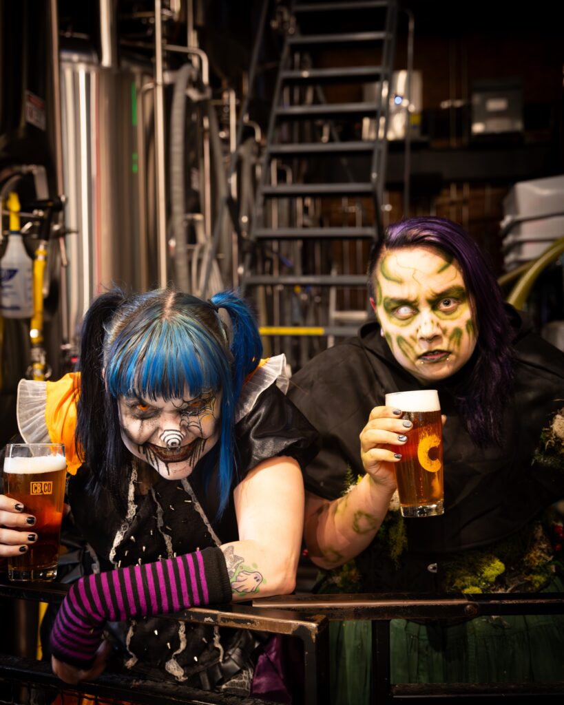 Two Hundred Acres Manor characters in full makeup holding Cinderlands beers in the brewery