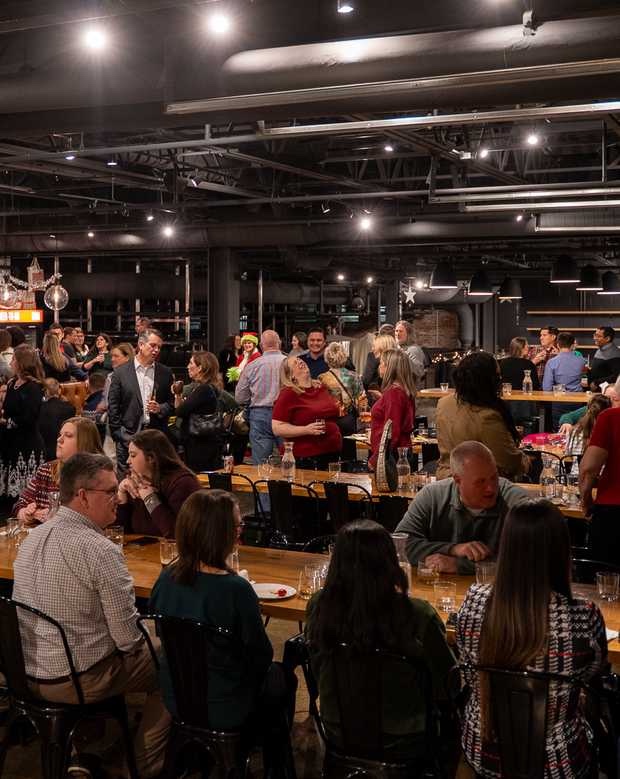 A company holiday party on the Upper Level of the Cinderlands Warehouse, guests at long tables and mingling